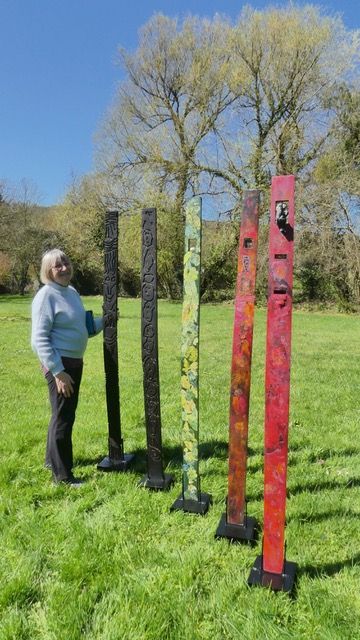 Cinq grandes douelles peintes, gravées et brûlées, dressées sur socle dans un jardin